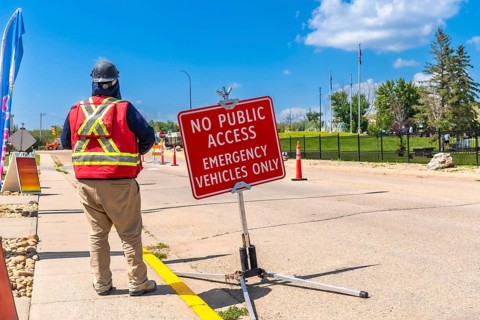 Construction worker wearing a safety vest and hardhat, standing near a no public access sign,