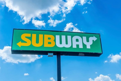 Green and yellow sandwich restaurant sign with white arrow pointing towards restaurant entrance