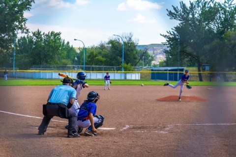 Young baseball pitcher throwing a ball during an intense game, while the batter, catcher, and
