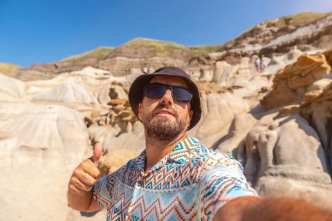Happy tourist wearing sunglasses and a bucket hat giving a thumbs up while taking a selfie in front