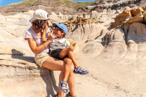 Mother holds her son on her lap, applying sunscreen to his nose during a sunny day exploring the