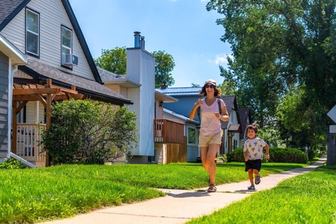 Mother and young son running joyfully on a sidewalk in a sunny, residential neighborhood,