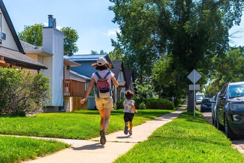 Mother with backpack and her son are running down a sidewalk in a residential area of drumheller,