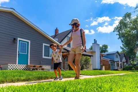 Happy mother and son holding hands and walking on a sidewalk in a residential neighborhood on a