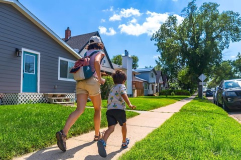Mother with backpack and her son are running on the sidewalk in a residential area of drumheller,