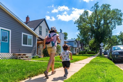 Mother with backpack and her son are running on the sidewalk in a residential neighborhood in