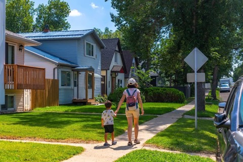 Mother and her young son are enjoying a leisurely stroll along a sidewalk in a quiet residential
