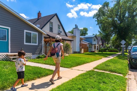 Enjoying a sunny summer day, a mother and her young son stroll along a quiet sidewalk in a charming