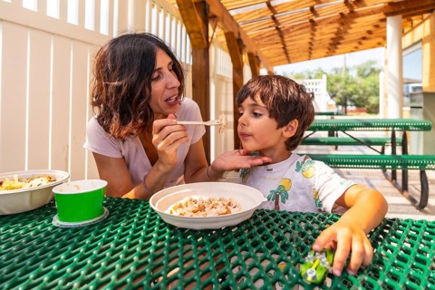 Mother feeds her son at a picnic table outside a restaurant in drumheller, alberta, canada,