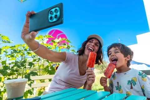 Mother and her son are sitting at a turquoise picnic table, holding popsicles and taking a selfie