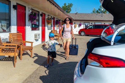 Happy mother pulling a suitcase while her cheerful son runs alongside, playing with toy cars,