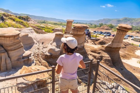 Tourist wearing a cap observing stunning hoodoo rock formations in drumheller valley, alberta,