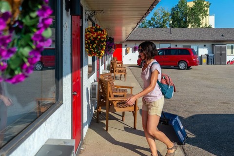 Female tourist is walking to her motel room pulling her wheeled suitcase, carrying a backpack and