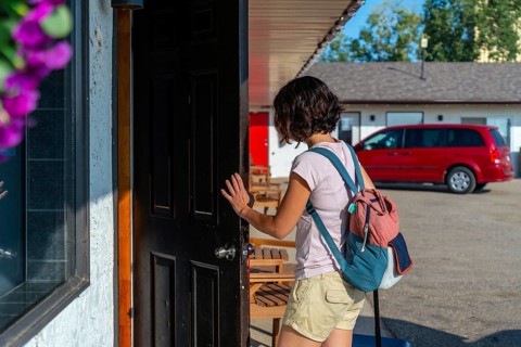Female tourist with a backpack and rolling suitcase opening the door to a motel room after a long