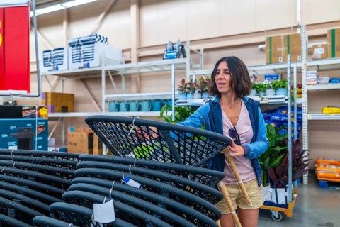 Smiling female customer selecting new outdoor furniture, picking up hanging egg chair in warehouse,