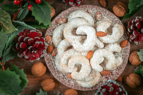 Vanilla croissants on a plate surrounded by walnuts, almonds and Christmas decorations