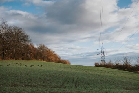 Meadow with a power pole on the horizon under a wide sky with large cloud formations, Ternitz,
