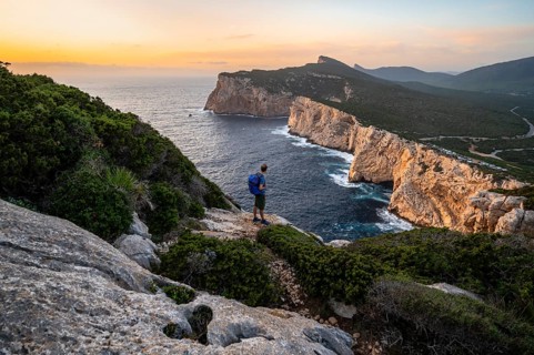 Tourist in front of coastal landscape at sunset, steep cliffs by the sea, cliffs in the evening