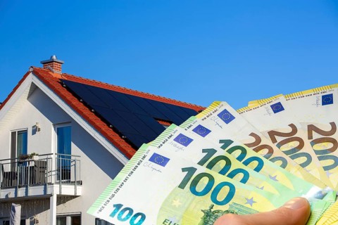 (Photo montage) Man holding euro banknotes in front of a solar roof
