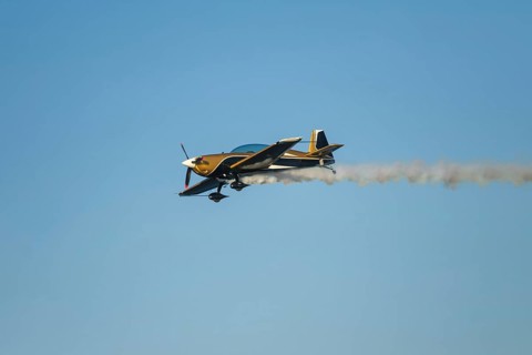 Golden stunt aerobatic plane performing stunts in blue sky with smoke trail. Concept of speed,