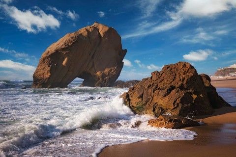 Penedo do Guincho, a large boulder rock arch at Praia da Santa Cruz, Portugal, with ocean waves and