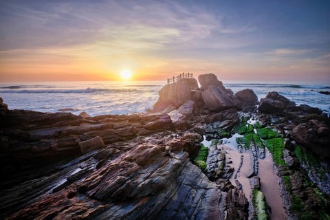 Scenic rock formation at Praia da Santa Cruz, Portugal, with ocean waves and vibrant sunset sky