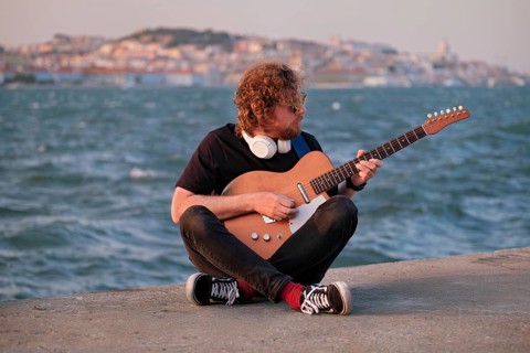 Hipster street musician in black playing electric guitar in the street on sunset on embankment with