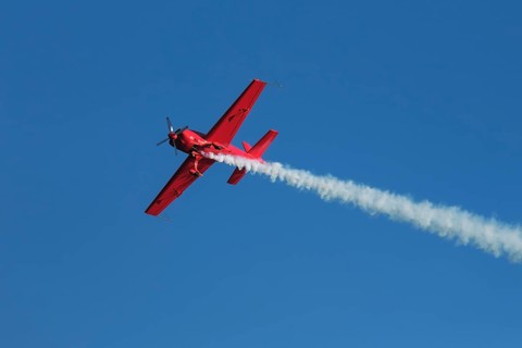 Red stunt aerobatic plane performing stunts in blue sky. Concept of speed, difficulty, precision,