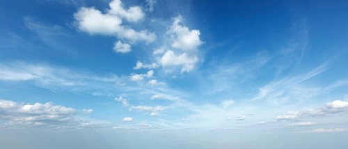 A tranquil sky filled with soft clouds under bright blue hues creates a peaceful daytime scene,