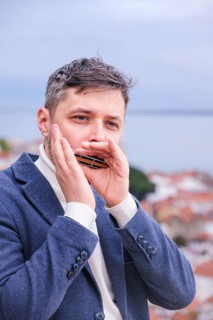 Man musician in a blue blazer and white sweater playing blues on a harmonica with eyes closed,