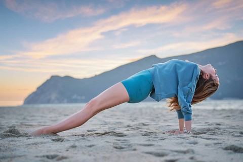 A woman practices Purvottanasana, or upward plank pose, on the beach during sunset. The golden sky