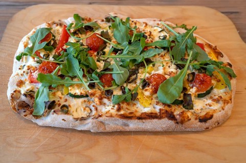 Pizza with goat cheese, tomatoes and arugula served on a wooden board, Ahrenshoop, DarÃŸ,