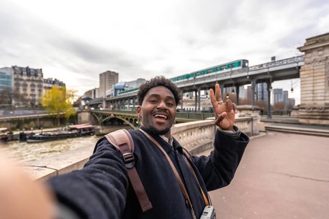 Happy african american man tourist taking a selfie portrait on a bridge over the seine river in