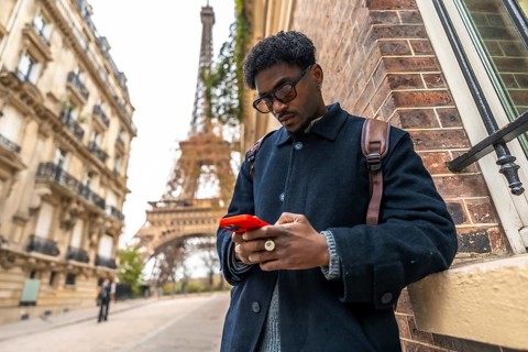 Young black man in paris leaning against a building, focusing on his smartphone, representing