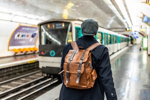 Man with backpack and flat cap standing on a subway platform, watching a train arriving,