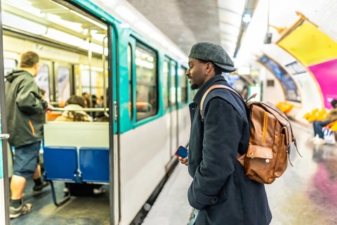 Young man stands on a bustling paris metro platform, looking toward an open train door as