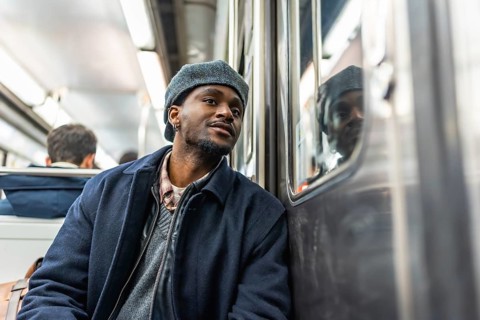 Young man sitting on a subway train, looking thoughtfully out the window during his daily commute,