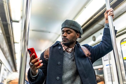 African american man on subway train holding a pole and browsing his smartphone during a commuting