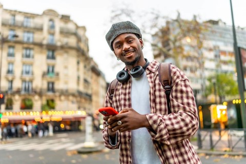 Young african man with a beret and headphones smiling at the camera while checking his smartphone,