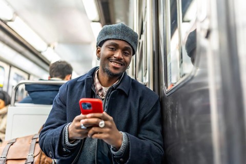 Young black man with a stylish hat smiling and looking at the camera while commuting on a subway
