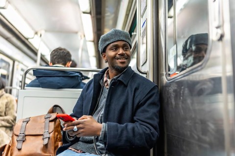 Young black man traveling on public transport, smiling and holding a smartphone, showcasing urban