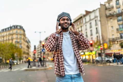 Young handsome black man walking a sunny european city street, smiling while listening to wireless
