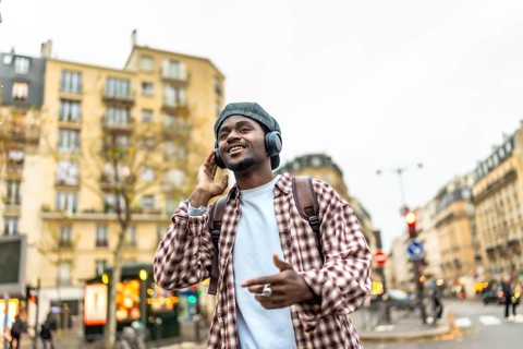 Young african man smiling and listening to music with headphones while walking in a bustling