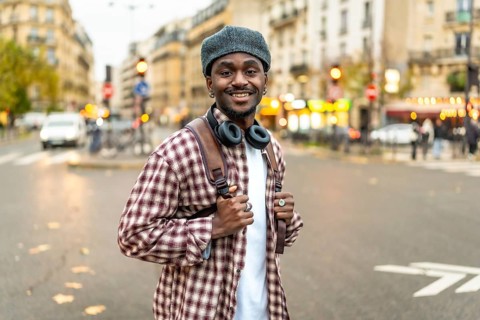 Young black man with headphones wearing a plaid shirt and backpack, standing confidently in a