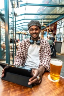 Young black man smiling, wearing headphones and a plaid shirt, looking at the camera while sitting