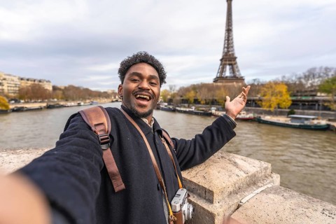 Young male tourist smiling and gesturing with open hand, capturing a memorable selfie while