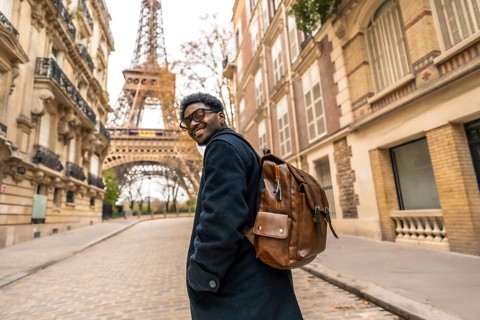 Young man smiling and turning back while exploring a historic street in paris, enjoying his leisure