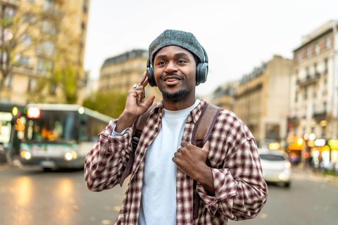African american man feeling happy listening to music on headphones while exploring a european city