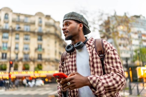 Young man using a smartphone and wearing headphones, a backpack, and a casual plaid shirt while
