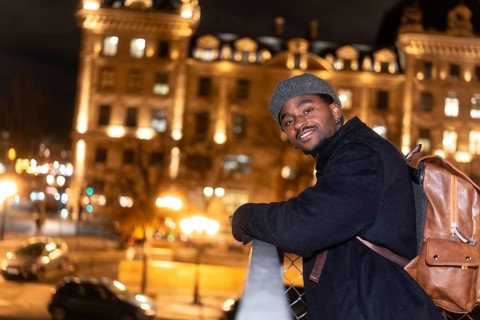 Young man smiling, wearing a beret, coat and backpack, viewing the illuminated city of paris at